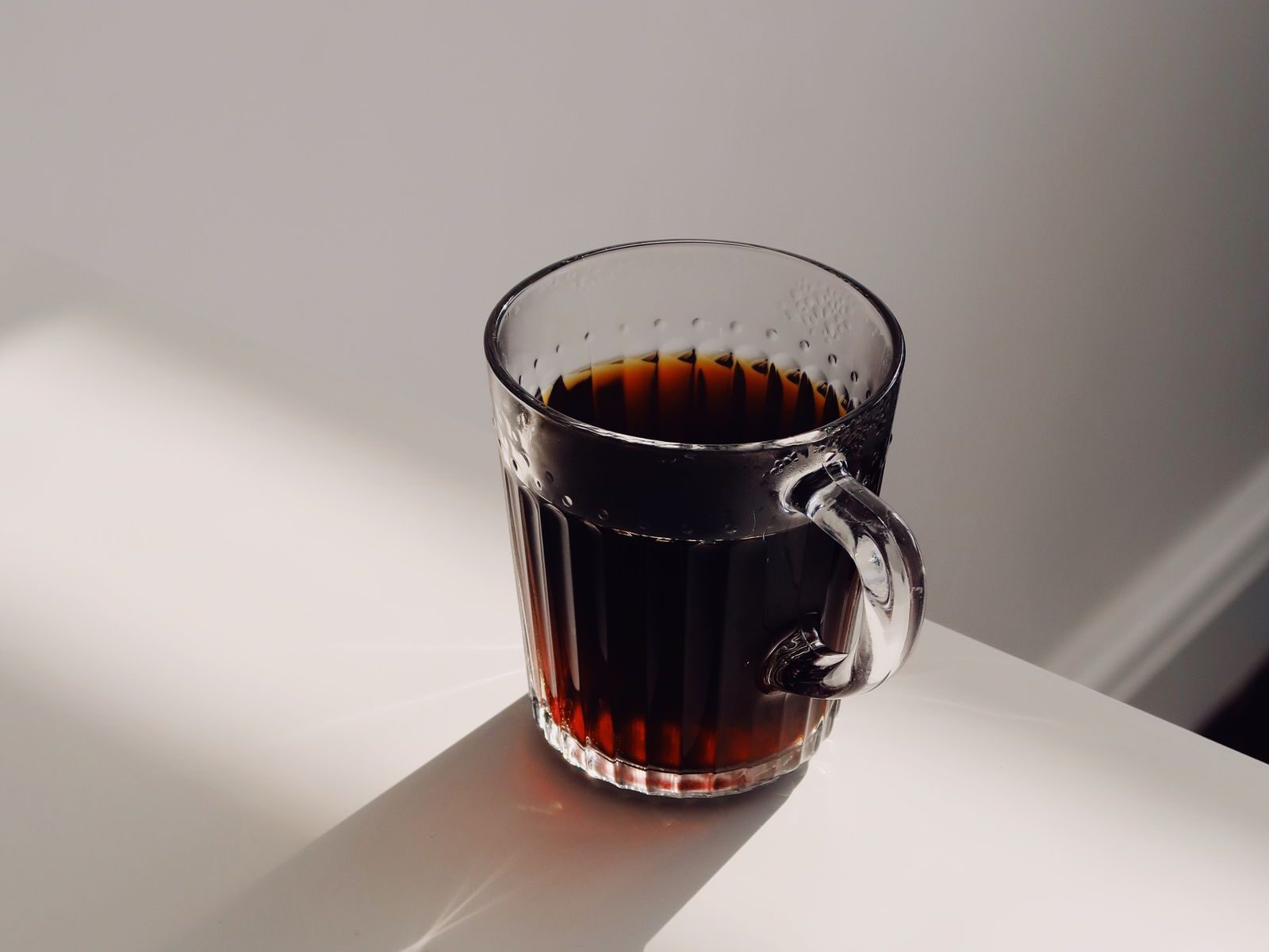 Glass cup of dark red-brewed black tea on a white surface