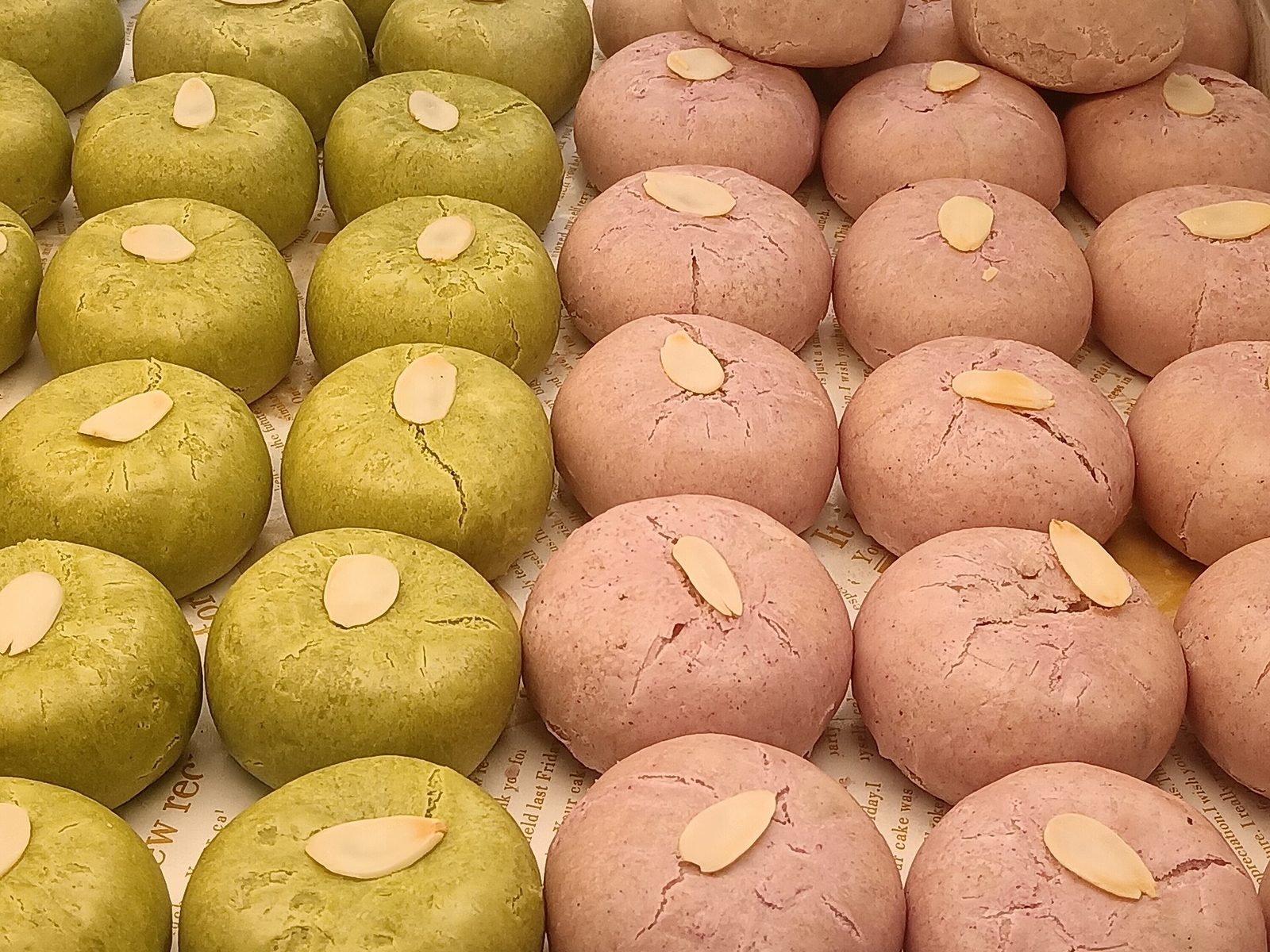 Green and pink round tea pastries topped with almond slices
