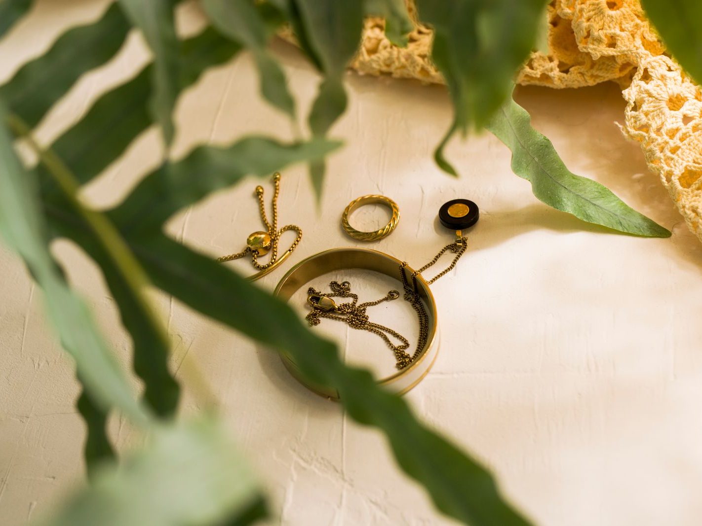 Gold jewelry pieces — bangle, rings and chains — styled on a white surface